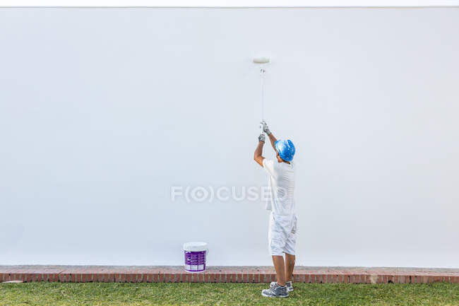 Giovane pittore irriconoscibile che dipinge la facciata di un appartamento con un rullo estensibile — Foto stock