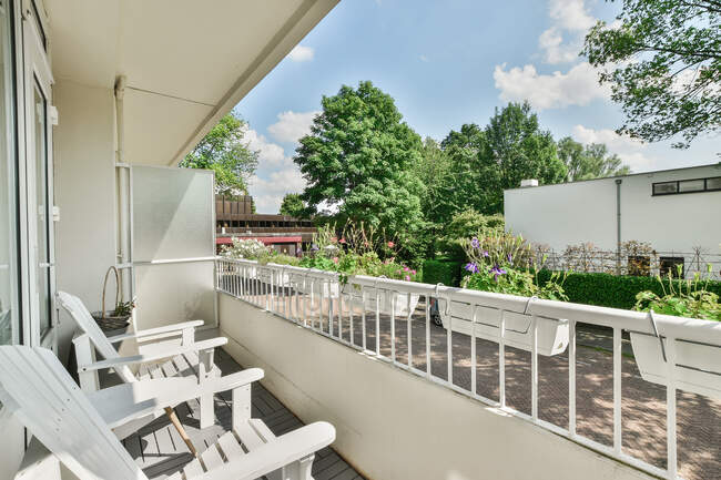Immeuble résidentiel moderne avec fauteuils et table sur balcon clôturé avec plantes en pot sous un ciel bleu nuageux à Amsterdam — Photo de stock