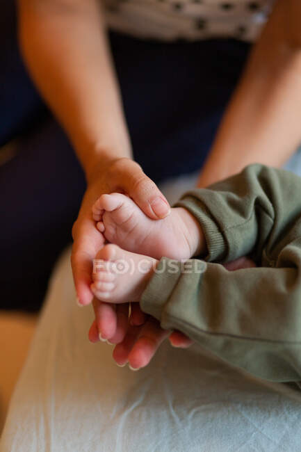 From above of crop anonymous mother massaging small feet of adorable barefoot baby lying on bed in sunny morning — Stock Photo