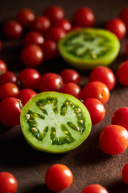 Sliced of unripe berry of Solanum lycopersicum plant with scattered cherry tomatoes — Stock Photo