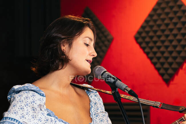 Confident lady with guitar singing in mic while performing song in bright club — Stock Photo