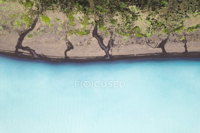 From above of still water of blue lake near stony coast with cracks and green vegetation in nature of Iceland on summer day — Stock Photo