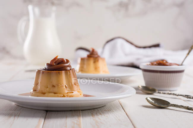 Eierpudding garniert mit süßen Dulce de leche auf weißen Tellern auf dem Tisch mit Besteck in der Küche — Stockfoto