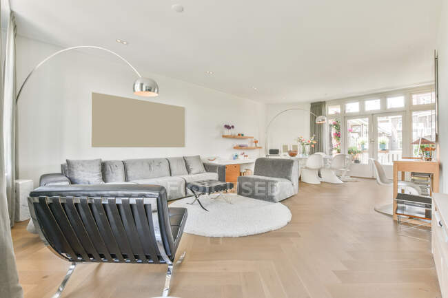 Poltrone e divano posti in luminoso soggiorno vicino sala da pranzo con tavolo e sedie in moderno appartamento con finestra — Foto stock
