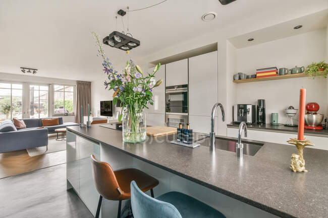 Ваза с цветами помещается на прилавок в современной кухне рядом с просторной гостиной на дому — стоковое фото