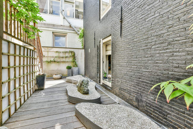 Hinterhof mit grünen Pflanzen und Steinelementen in der Nähe von grauem Backsteingebäude am Tag platziert — Stockfoto