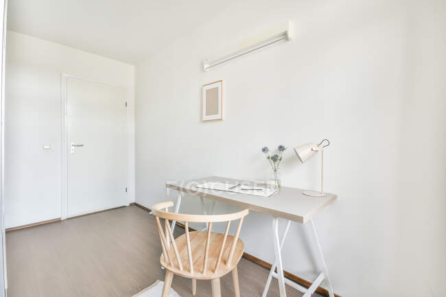 Table simple avec lampe chaise en bois placée dans la salle de travail avec murs blancs et parquet dans l'appartement — Photo de stock