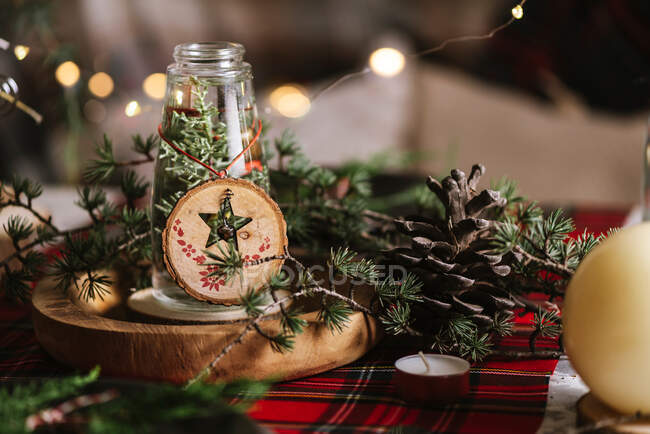 Різдвяний стіл з вінком та декоративними дерев'яними прикрасами та червоною картатою скатертиною з жовтими вогнями на фоні — стокове фото