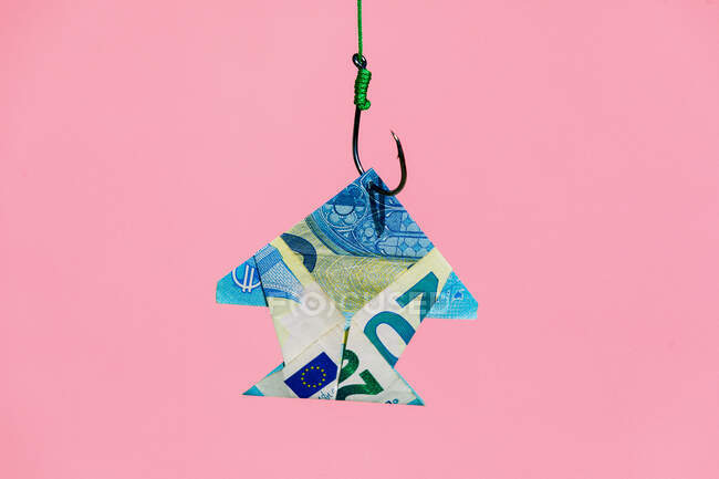 Банкнота у формі риби, що висить на металевому гачку з зеленою мотузкою на рожевому фоні у світлій сучасній студії — стокове фото