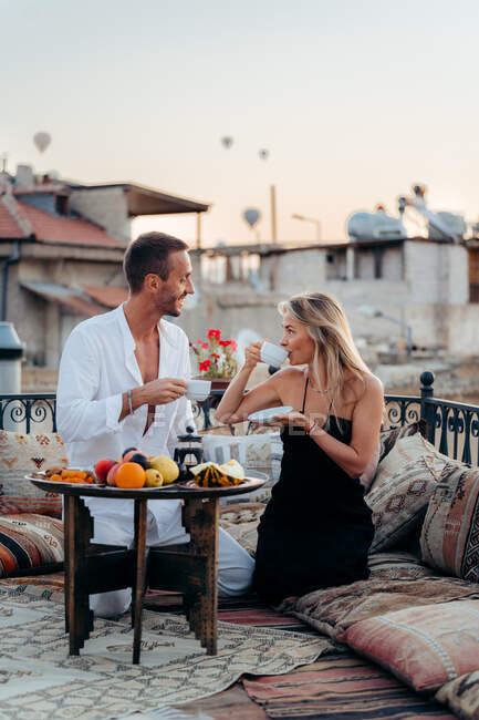 Zufriedene Männer und Frauen, die Tee trinken und einander anschauen, während sie Zeit miteinander auf der Terrasse des Cafés mit Kissen in der Türkei verbringen Kappadokien — Stockfoto