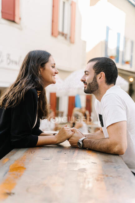 Seitenansicht eines romantischen jungen hispanischen Paares, das sich Händchen hält und sich glücklich anschaut, während sie am Tisch im Straßencafé sitzen — Stockfoto