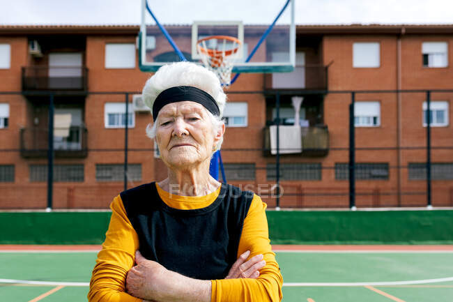 Mujer madura de confianza en ropa deportiva con la nariz perforada mirando a la cámara mientras está de pie en el campo de deportes durante el entrenamiento en la calle - foto de stock