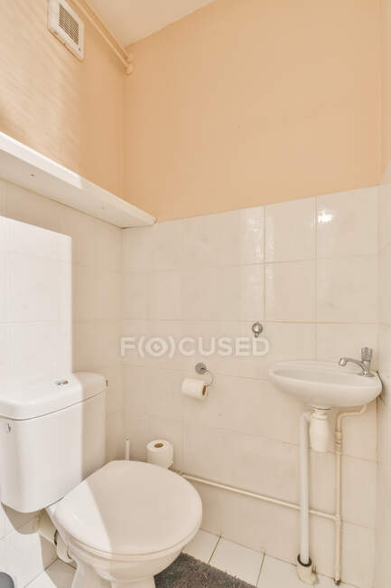 Інтер'єр сучасного туалету з жовтими пофарбованими стінами і білою плиткою, запакованою білим туалетом і раковиною з краном в яскраве денне світло — стокове фото
