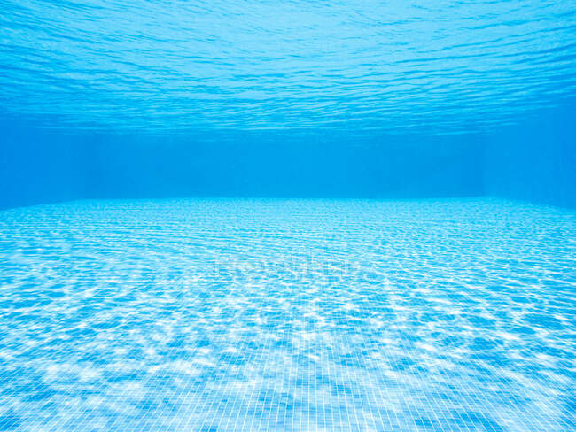 Blue swimming pool with glowing water with ripples above tiled bottom on sunny day — Stock Photo