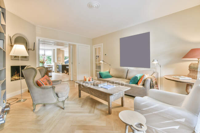 Design creativo della stanza con tavolo tra poltrone e divano con cuscini contro il camino in casa luce — Foto stock