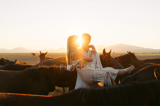 Uomo che tiene fiera fidanzata dai capelli tra i cavalli in campagna pascolo mentre si guarda l'un l'altro — Foto stock