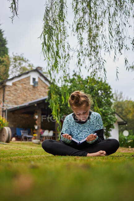 Тіло концентрованої босоногої дівчини читає цікаву книжку, сидячи на трав 