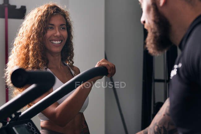 Culturistas musculosos confiados con tatuajes que hablan contra la deportista alegre en el gimnasio durante el día - foto de stock