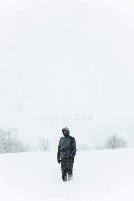 Чоловік у теплому зовнішньому одязі стоїть у сніговій долині проти голих дерев під час хуртовини холодного зимового дня в Мадриді. — стокове фото