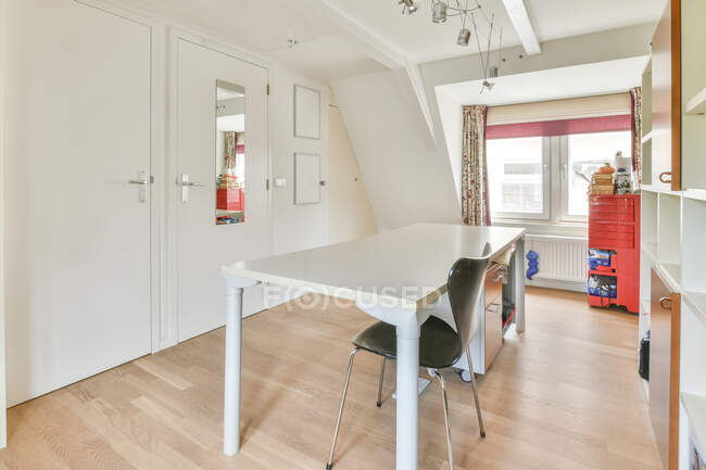 Innenraum des hellen Zimmers mit weißem Tisch und Schrank mit Regalen in der Wohnung bei Tageslicht — Stockfoto