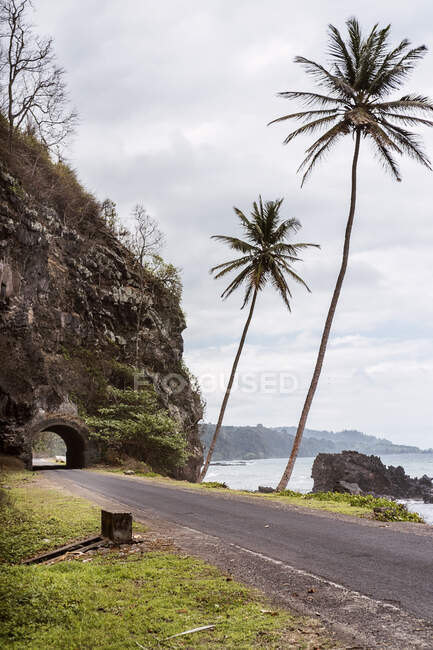 Pittoresco paesaggio di strada asfaltata vuota che attraversa scogliera rocciosa lungo la costa dell'oceano in modo Tom e Prncipe sotto cielo nuvoloso di giorno — Foto stock