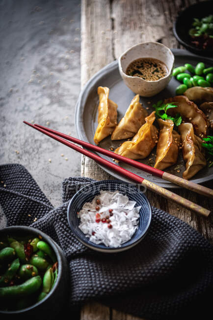 Gyozas with green beans and soy sauce with sesame seeds placed with chopsticks near bowls with spices and pea pods — Stock Photo
