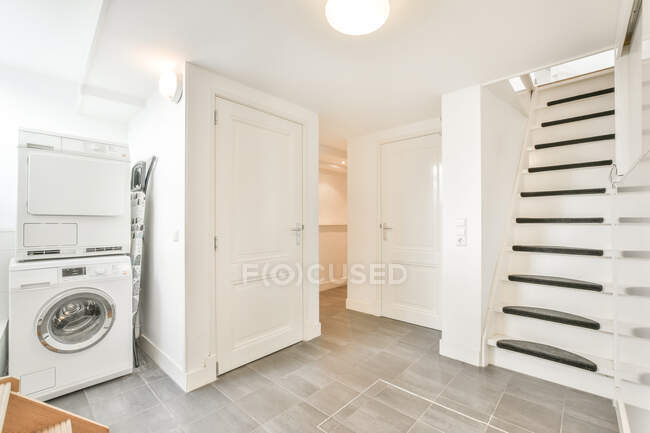 Design de interiores moderno de lavandaria contemporânea com máquina de lavar roupa perto da porta e escada no apartamento — Fotografia de Stock