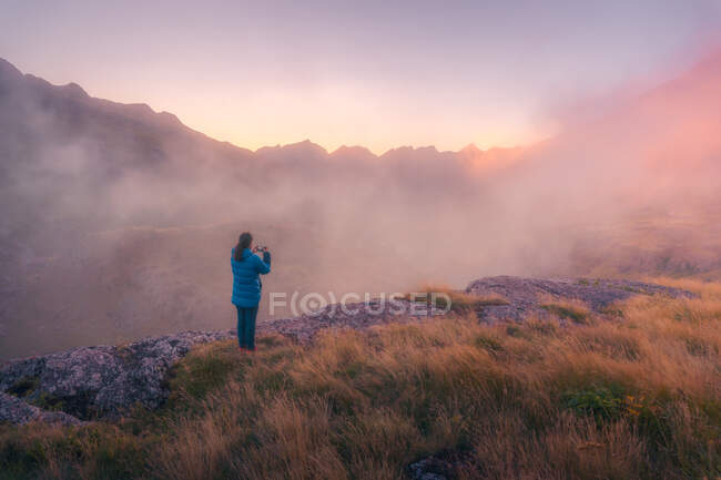 Обратный вид на далеких неузнаваемых туристов, стоящих на травянистой местности в окружении грубых гор в природе Испании в туманную погоду — стоковое фото