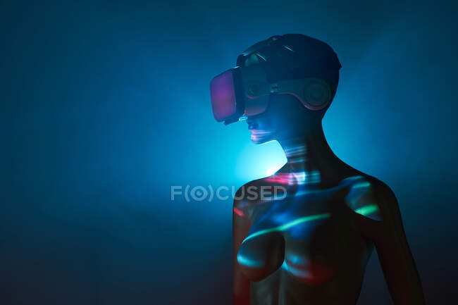 Манекен женщины в футуристических очках VR помещен под яркую проекцию в тусклом помещении — стоковое фото