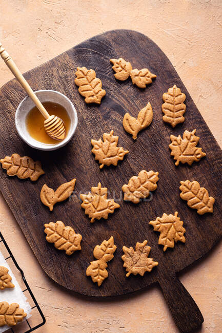 Top view abundance of leaf shaped sweet baked cookies placed on wooden cutting board near bowl of honey in kitchen — Stock Photo