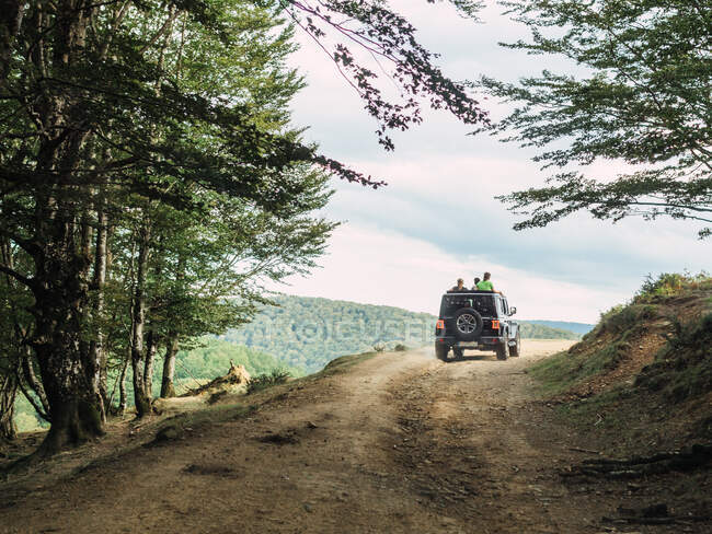 Vista posteriore di viaggiatori irriconoscibili in piedi in auto SUV guida lungo la strada accidentata durante il viaggio nella pittoresca valle montuosa — Foto stock