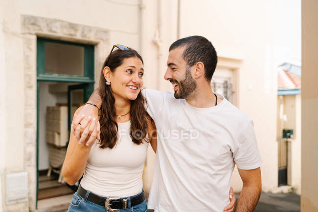 Fröhlich verliebtes junges hispanisches Paar in lässiger Kleidung lacht, während sie auf der Straße in der Stadt spazieren — Stockfoto