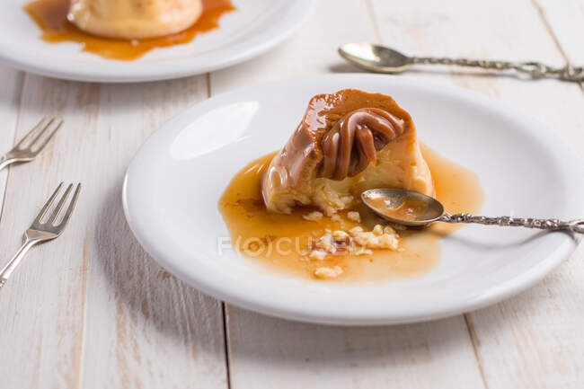 Fresh egg custard topped with sweet dulce de leche served with syrup on wooden table with cutlery in kitchen — Stock Photo