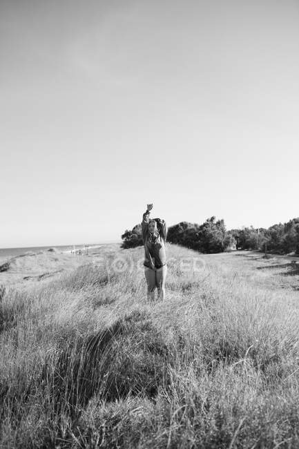 Black and white of anonymous female in shirt standing with raised arms on grassy meadow under cloudless sky in summer — Stock Photo