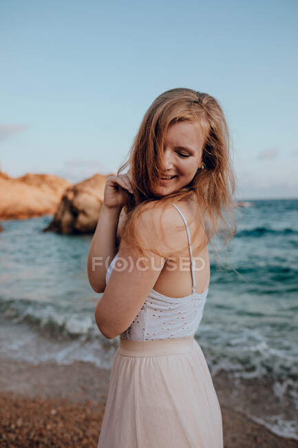 Attractive young female with long hair and closed eyes while standing on seashore in summer on blurred background — Stock Photo