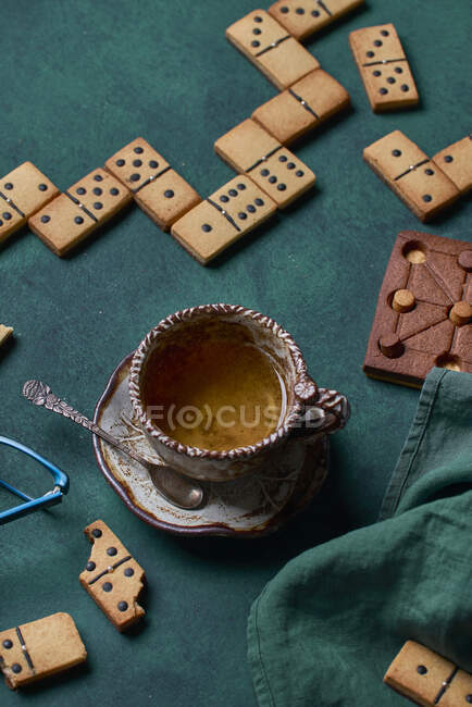Draufsicht auf leckere süße Domino-Kekse auf grünem Hintergrund mit Tasse Heißgetränk und Schokoladengebäck — Stockfoto