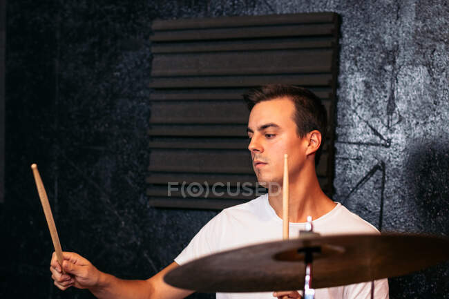 Сконцентрований молодий музикант у повсякденному одязі грає в краш-цимбал у яскравому клубі біля сірої стіни. — стокове фото
