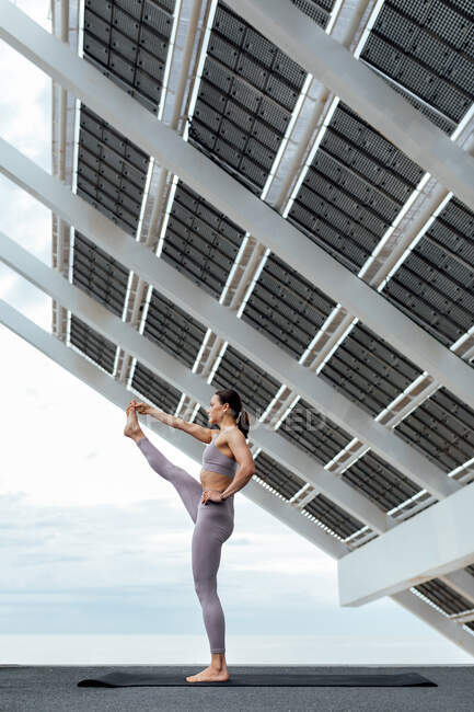 Full body side view of active female balancing while practicing Utthita Hasta Padangushthasana posture near modern solar panel in Barcelona — Stock Photo