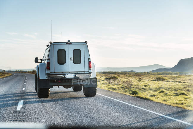 Modern large offroader car driving on empty asphalt road going through grassy fields in countryside under cloudless blue sky in sunny day — Stock Photo