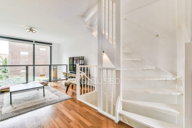 Escalier blanc près du salon spacieux avec table et télévision moderne dans un appartement élégant et lumineux avec grande fenêtre et clôture — Photo de stock
