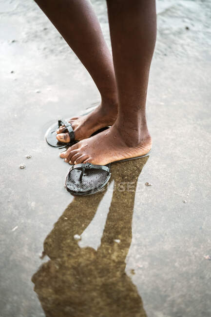 Над непізнаним чорним босоногим малюком, що стоїть у маленькій калюжі на асфальтній дорозі на острові Со Том і Принсіпі вдень. — стокове фото