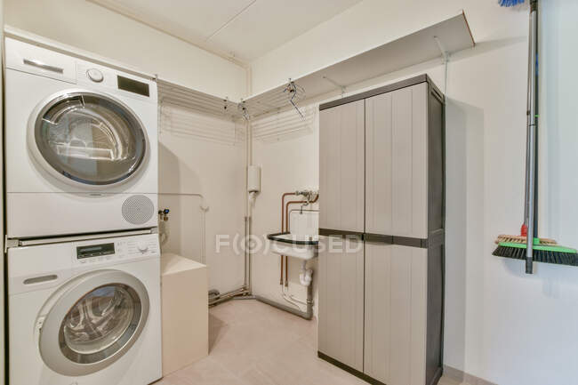 Creative design of laundry with washstand and cabinet against dryer with washer in light house — Stock Photo