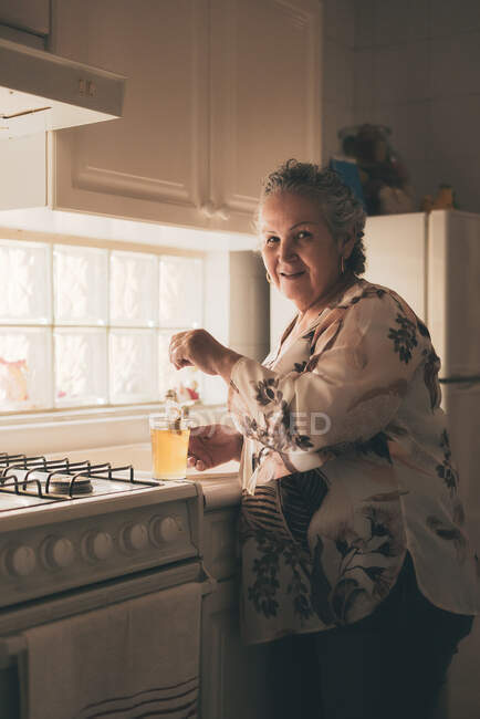 Sorrindo adulto feminino vestindo blusa de seda e calças de cerveja saco de chá na cozinha caneca de vidro — Fotografia de Stock