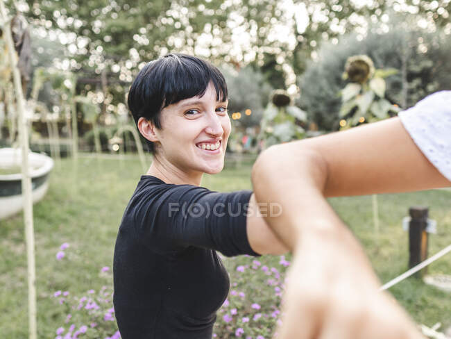 Lächelnde Frau stößt sich mit Erntefreunden beim Gruß im Sommergarten an den Ellenbogen — Stockfoto