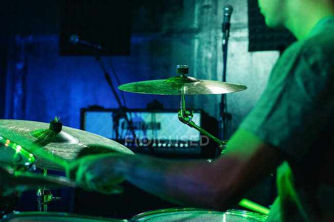 Обрізаний невідомий концентрований чоловічий музикант, який грає на барабанах у клубі з зеленим та синім неоновим освітленням — стокове фото