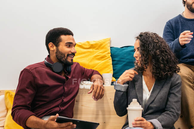 Concentrated young ethnic male employee talking to female colleague during break in modern coworking space — Stock Photo