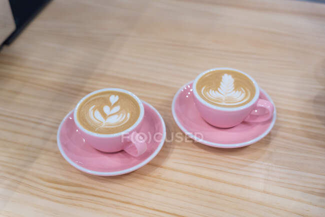Mugs of hot coffee with creative latte art served on plate with teaspoon on wooden table in modern light coffee house — Stock Photo