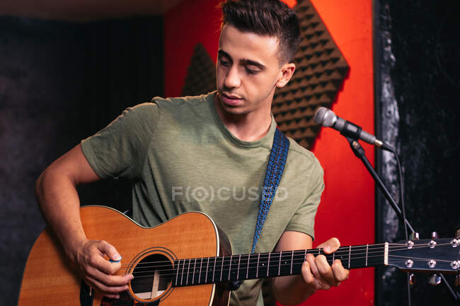Positive young male guitarist playing acoustic guitar and singing in microphone in light club — Stock Photo