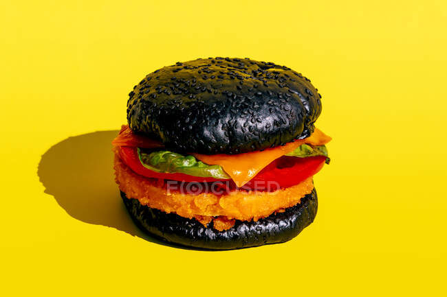 De cima hambúrguer fresco com pão preto e legumes no fundo amarelo — Fotografia de Stock