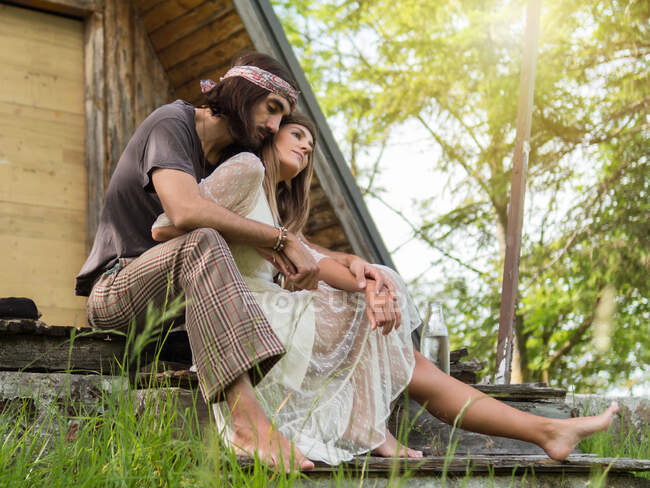 Casal hippie atraente abraçando nos degraus do alpendre na frente da cabine — Fotografia de Stock